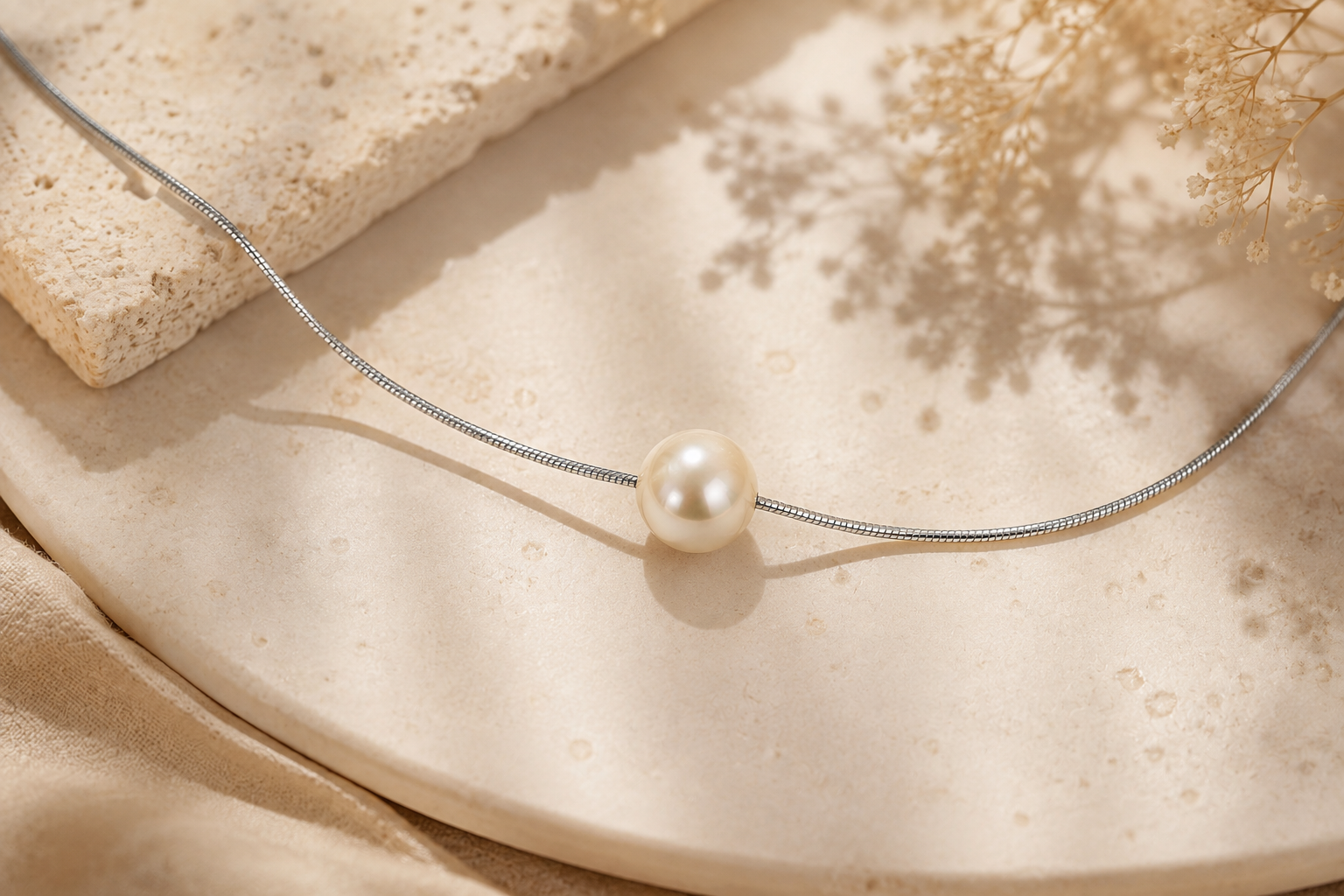 1mm platinum snake chain necklace with an 8mm vintage Japanese pearl, styled on warm natural stone in soft sunlight.
