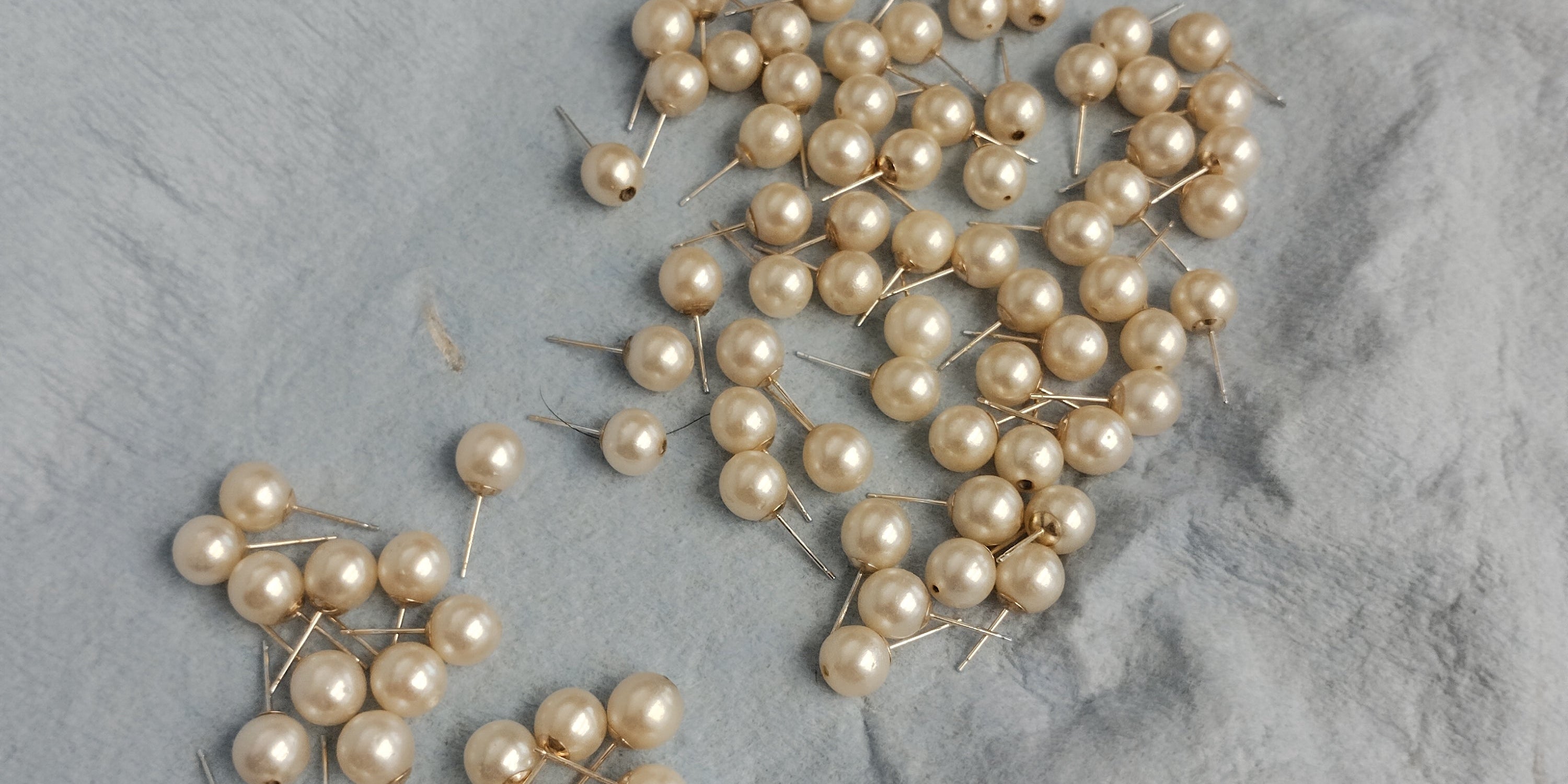 Cleaned natural pearls with mounted 10k yellow gold earring posts, showing visible top through-drilled holes prior to cap installation on a jeweler's bench at Motek Jewelry
