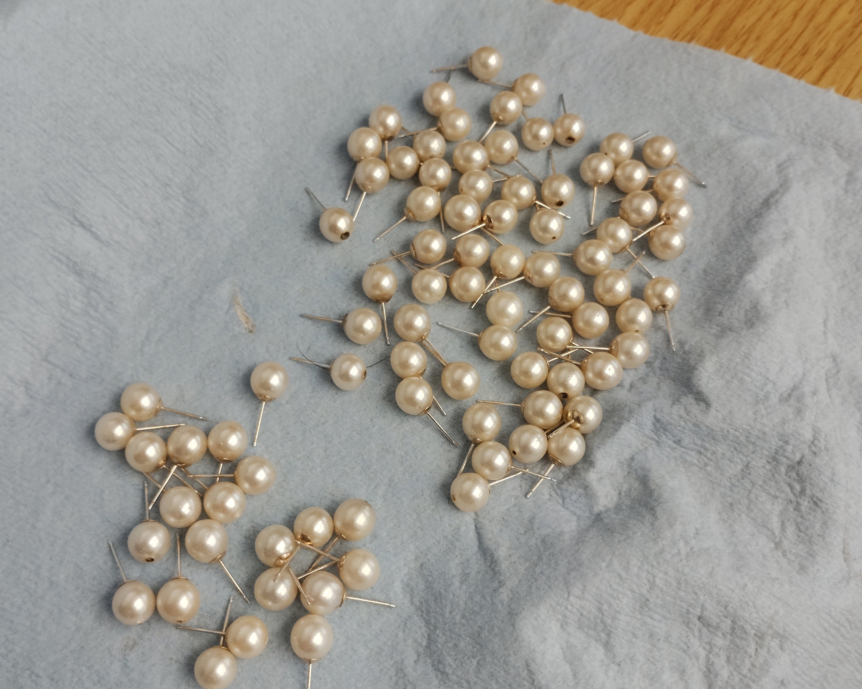 Cleaned natural pearls with mounted 10k yellow gold earring posts, showing visible top through-drilled holes prior to cap installation on a jeweler's bench at Motek Jewelry