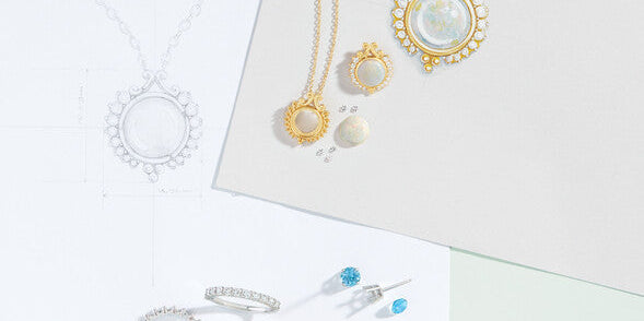 Custom jewelry design sketches, technical CAD blueprints, opal pendant necklaces, diamond eternity bands, and loose gemstones on a design desk at Motek Jewelry in Airmont NY