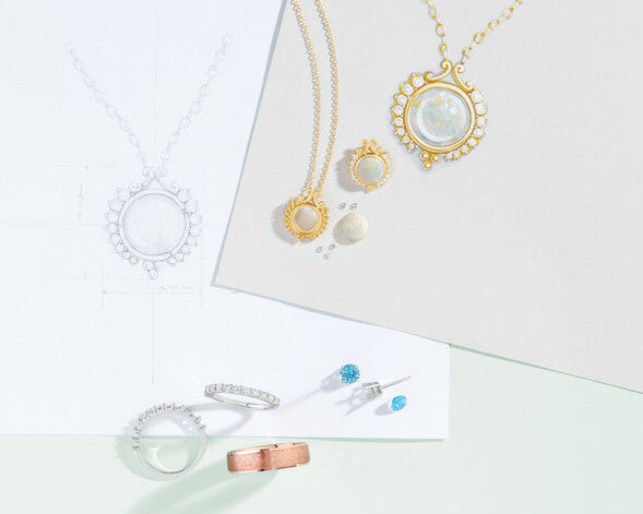 Custom jewelry design sketches, technical CAD blueprints, opal pendant necklaces, diamond eternity bands, and loose gemstones on a design desk at Motek Jewelry in Airmont NY