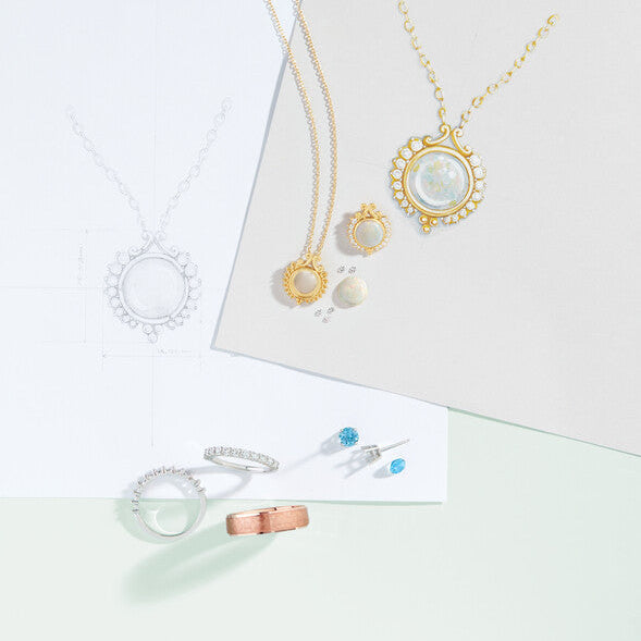 Custom jewelry design sketches, technical CAD blueprints, opal pendant necklaces, diamond eternity bands, and loose gemstones on a design desk at Motek Jewelry in Airmont NY