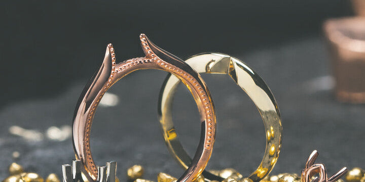Unmounted rose gold and yellow gold ring settings resting alongside a white gold prong head and raw gold nuggets on a dark bench stone at Motek Jewelry Design Studio in Airmont, NY.