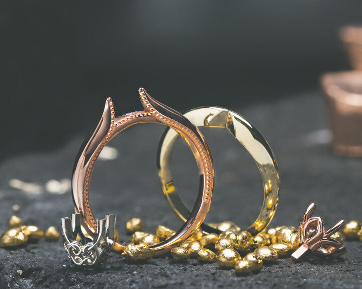Unmounted rose gold and yellow gold ring settings resting alongside a white gold prong head and raw gold nuggets on a dark bench stone at Motek Jewelry Design Studio in Airmont, NY.