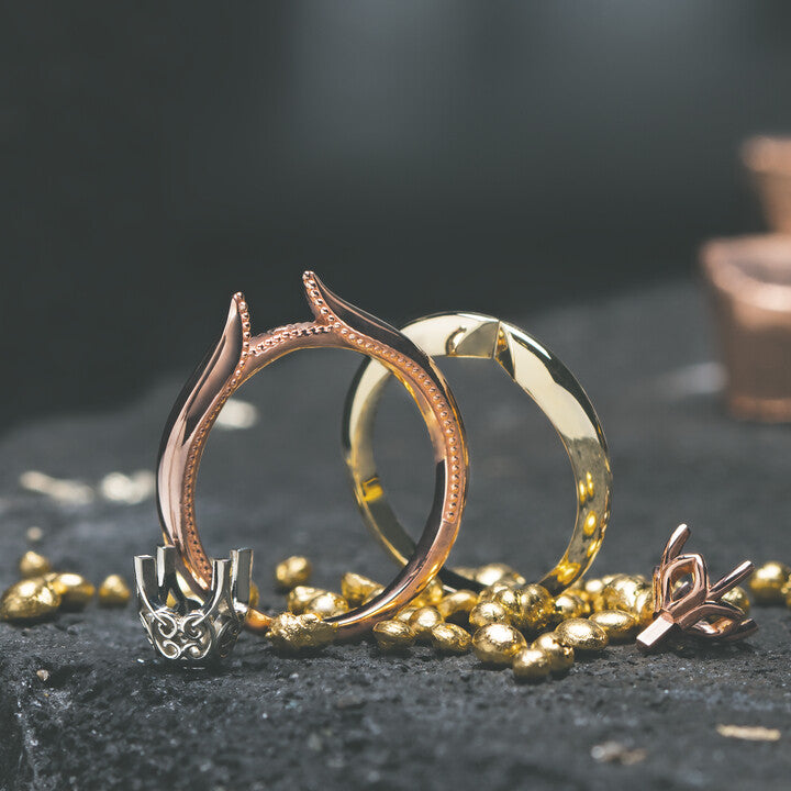Unmounted rose gold and yellow gold ring settings resting alongside a white gold prong head and raw gold nuggets on a dark bench stone at Motek Jewelry Design Studio in Airmont, NY.