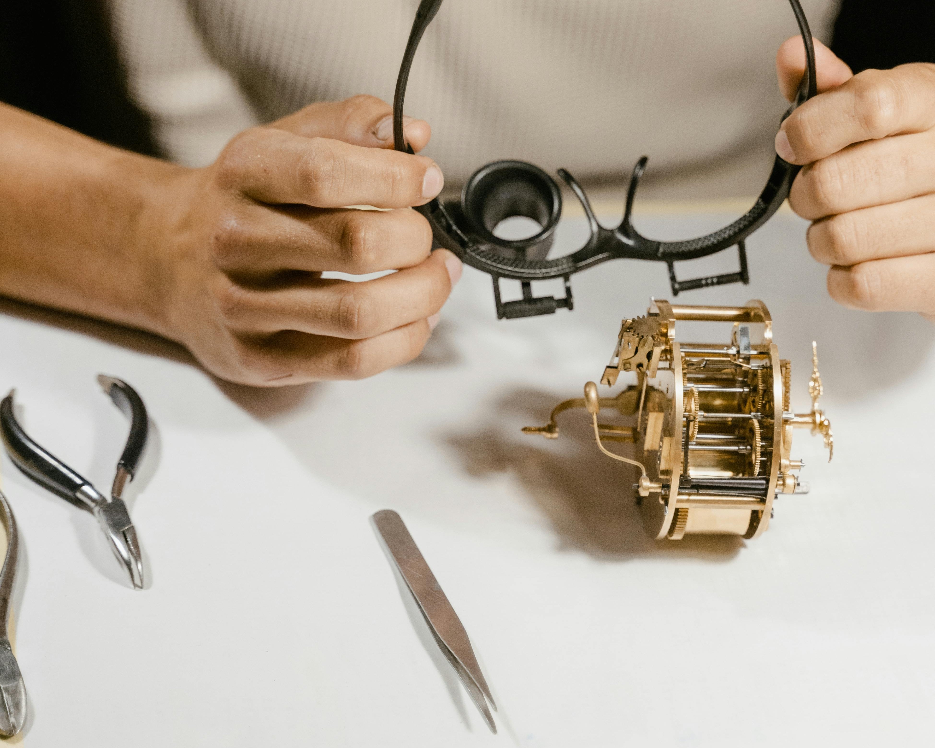 Image of a jeweler meticulously examining a piece of jewelry with tools (loupe, tweezers, scale) on a clean white background