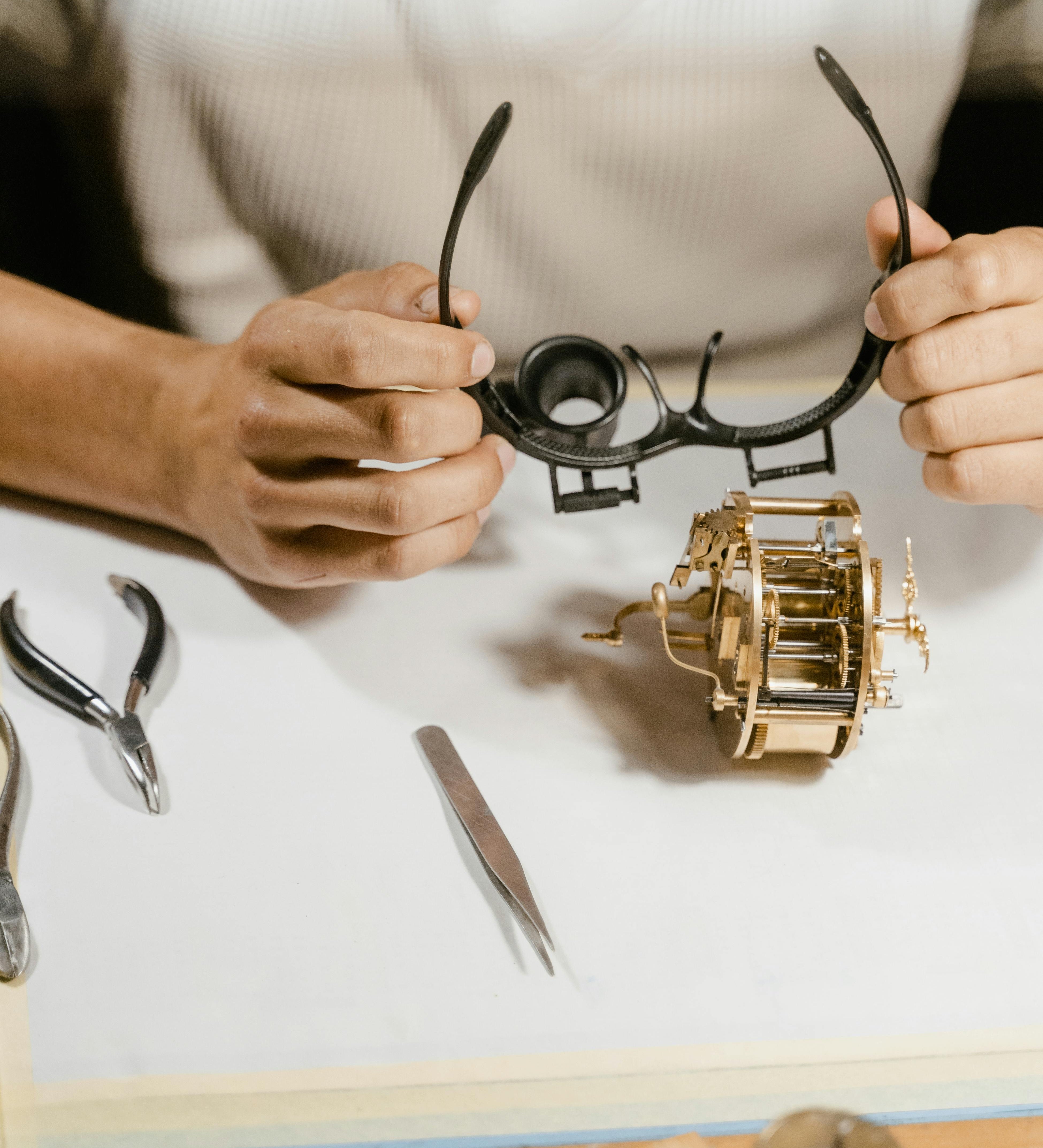 Image of a jeweler meticulously examining a piece of jewelry with tools (loupe, tweezers, scale) on a clean white background